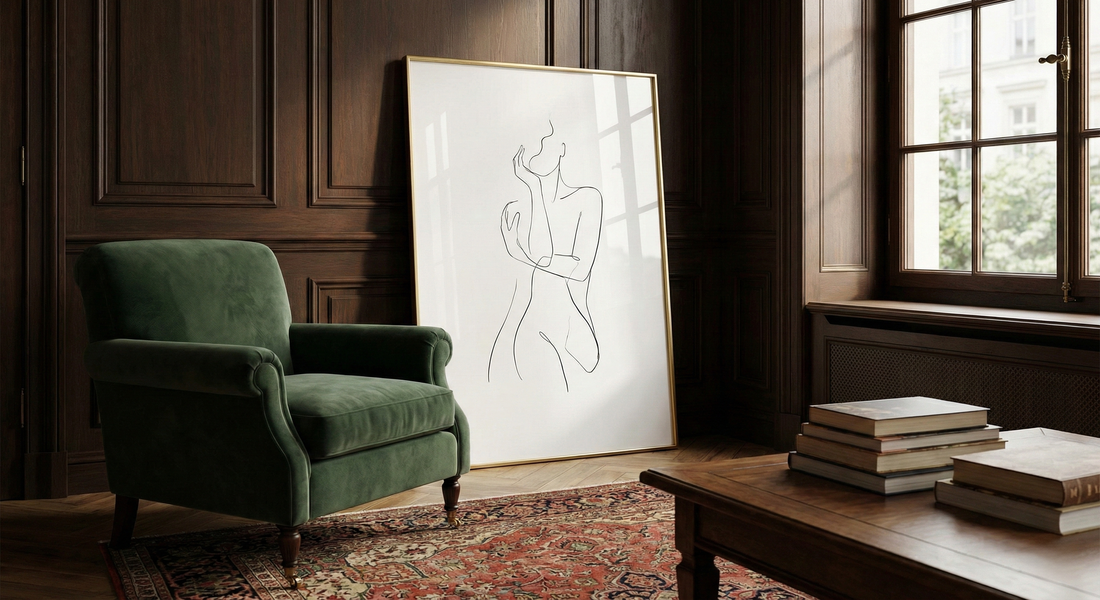Minimalist line art poster in gold frame beside green armchair in classic study room