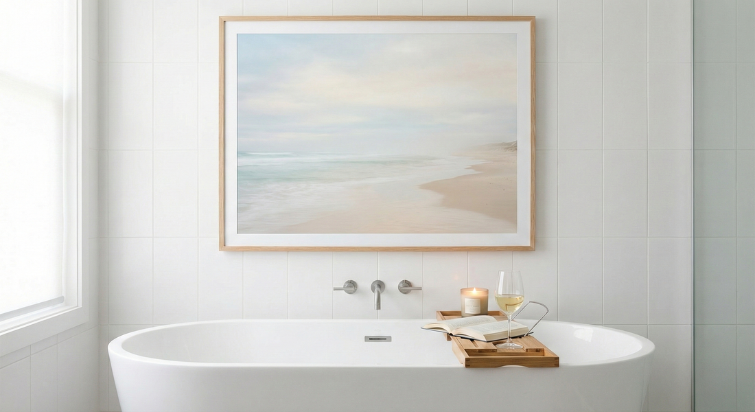Minimalist bathroom with white tub, ocean beach wall art, candle, book, and wine glass