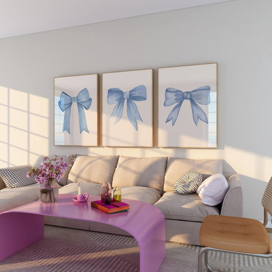 Modern living room with three blue bow wall art posters above a beige sofa, pink coffee table, and decorative accents