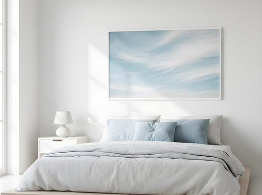 Minimalist bedroom with soft blue and white bedding, sky wall art, and natural sunlight