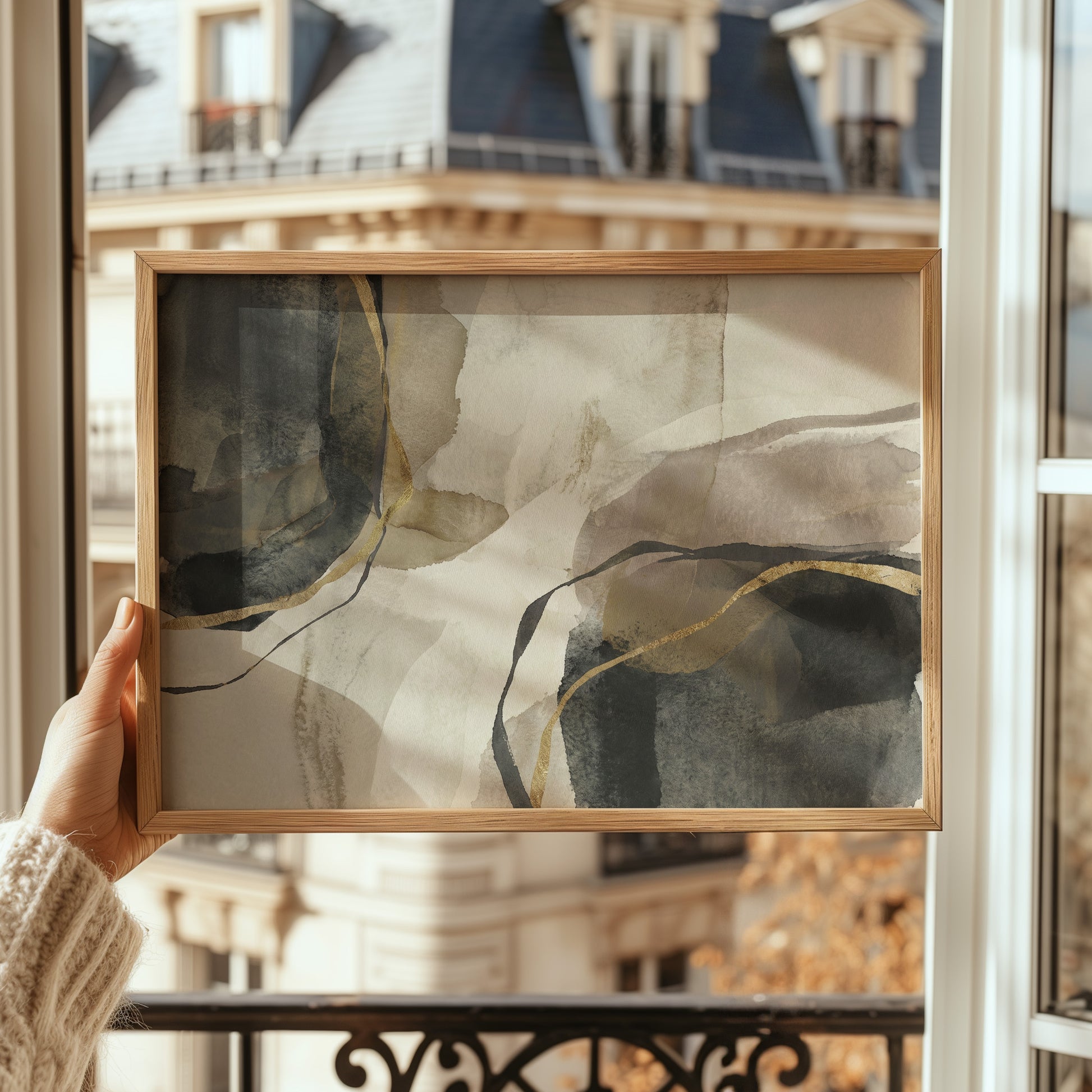 Person holding a framed abstract art piece with a blurred building exterior in the background